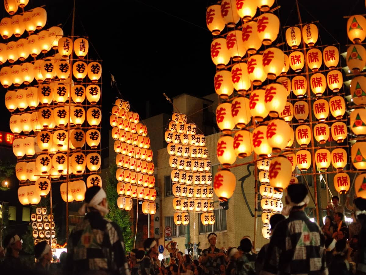 many lanterns lit up on tall poles in night parade at kanto matsuri