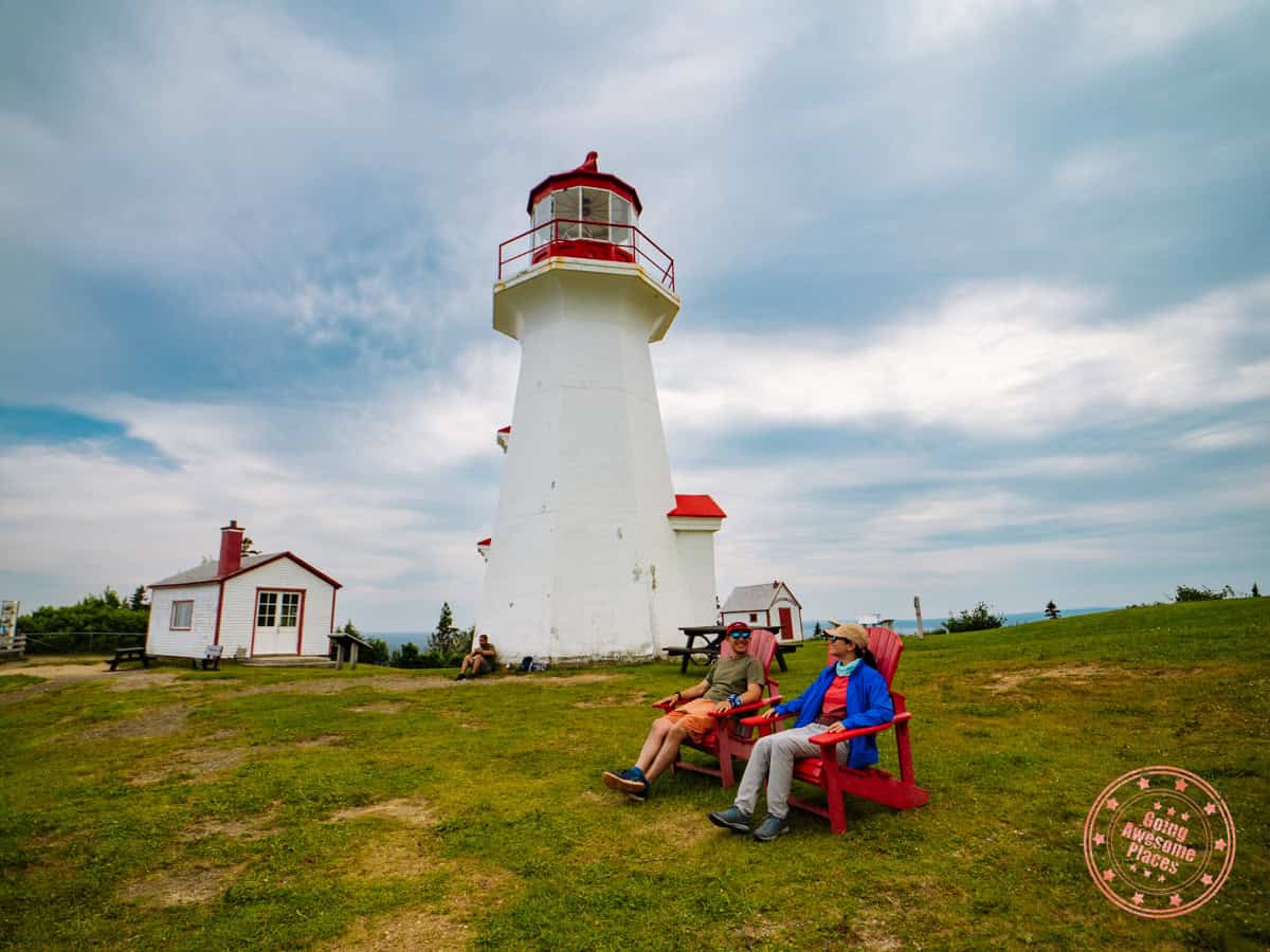 couple sitting on parks canada red chairs at cap gaspe lighthouse