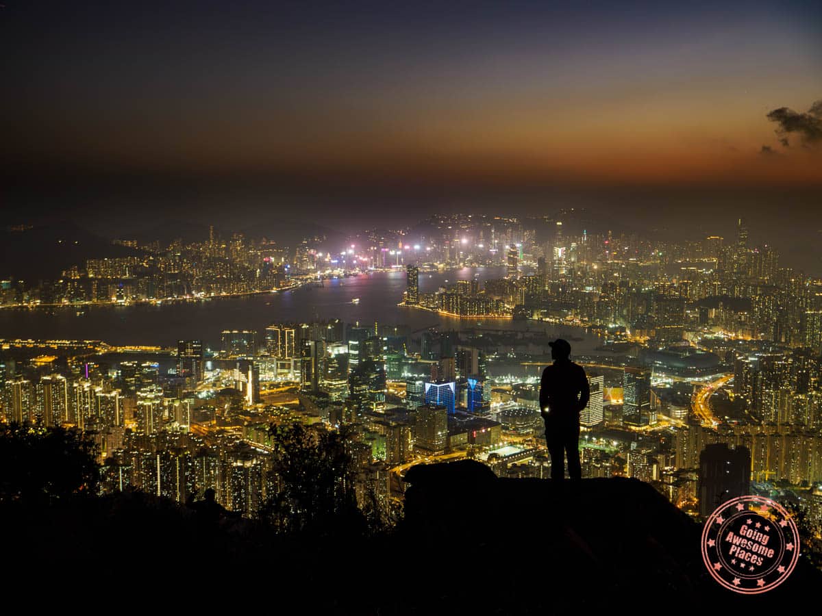 silhoette of man standing on rock on kowloon peak hike with view of the night skyline view of hong kong