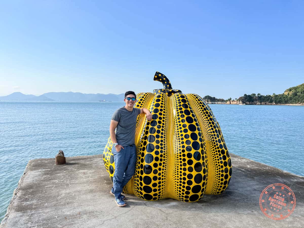 man standing with yayoi kusama's yellow pumpkin on naoshima island in japan