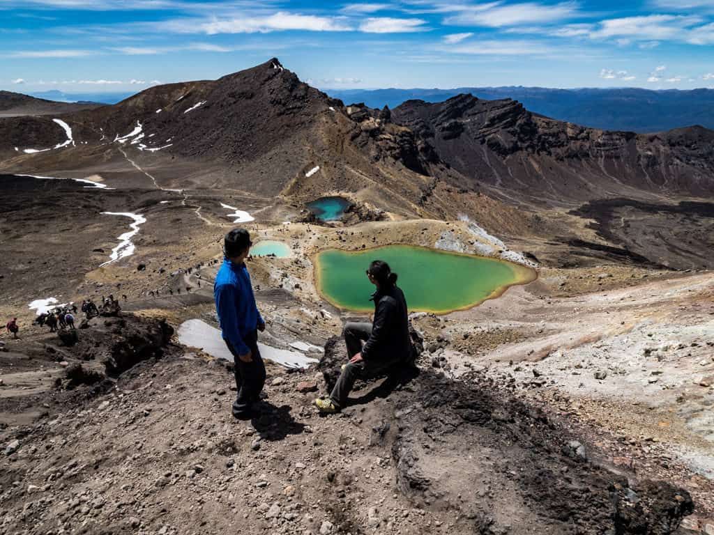 tongariro crossing with one male and one female hiker looking out towards emerald lakes below
