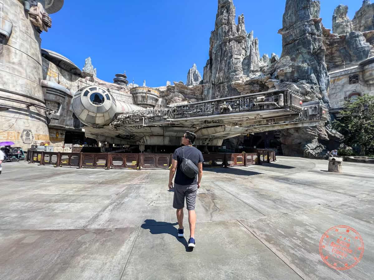 man walking in galaxy's edge spaceport with millennium falcon in the background