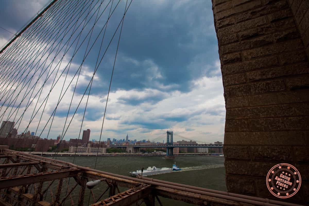 distant view of brooklyn bridge into city over boat in river